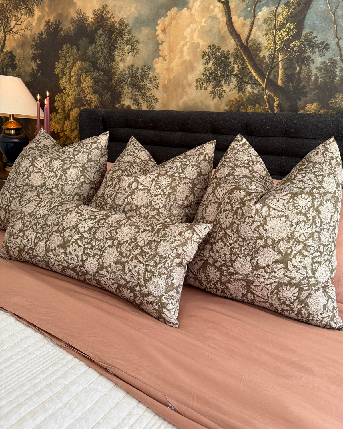 Decorative pillows with floral pattern on a bed against a scenic wall painting.